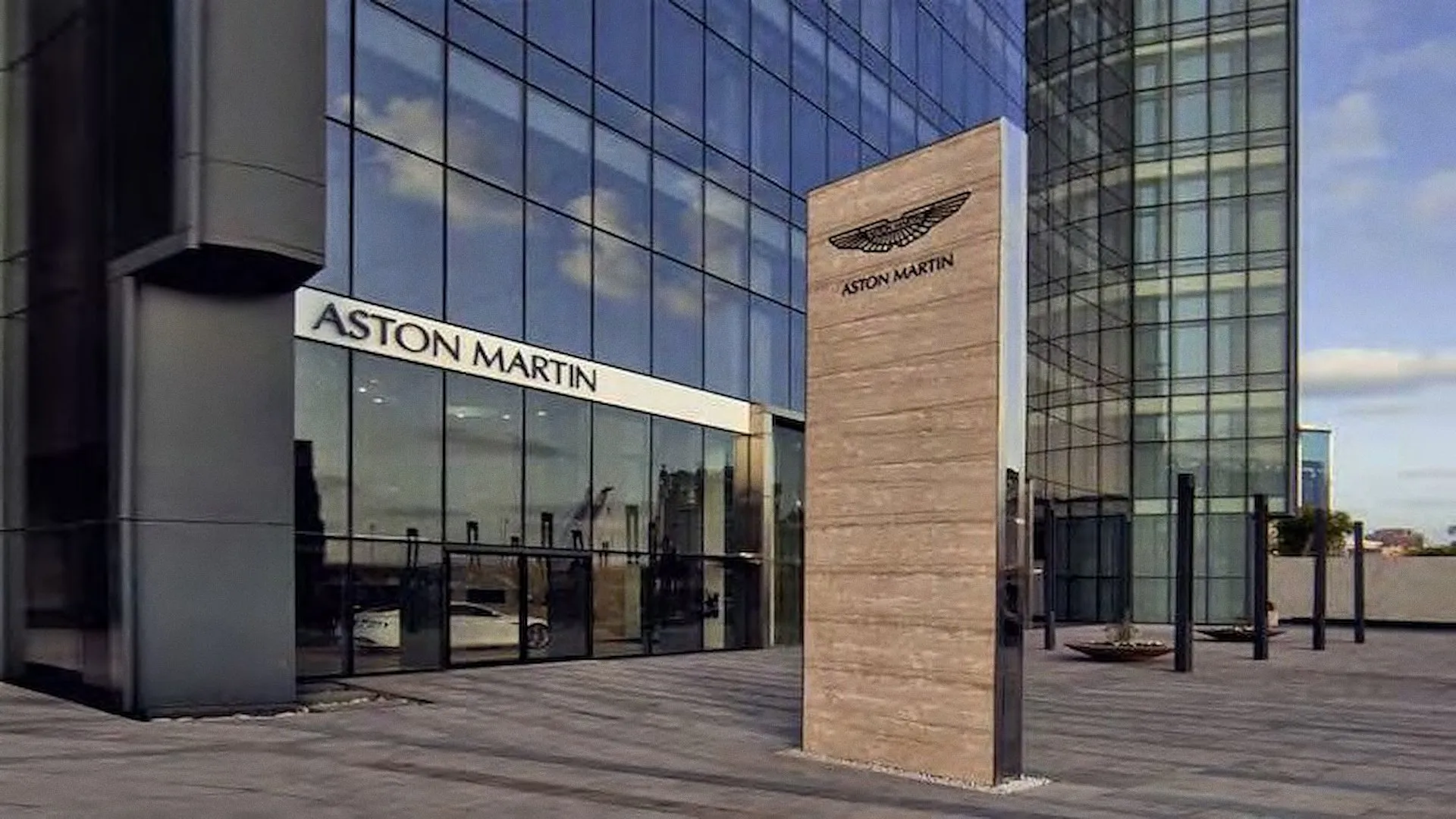 Aston Martin showroom entrance with a tall travertine pylon in front of the glass facade