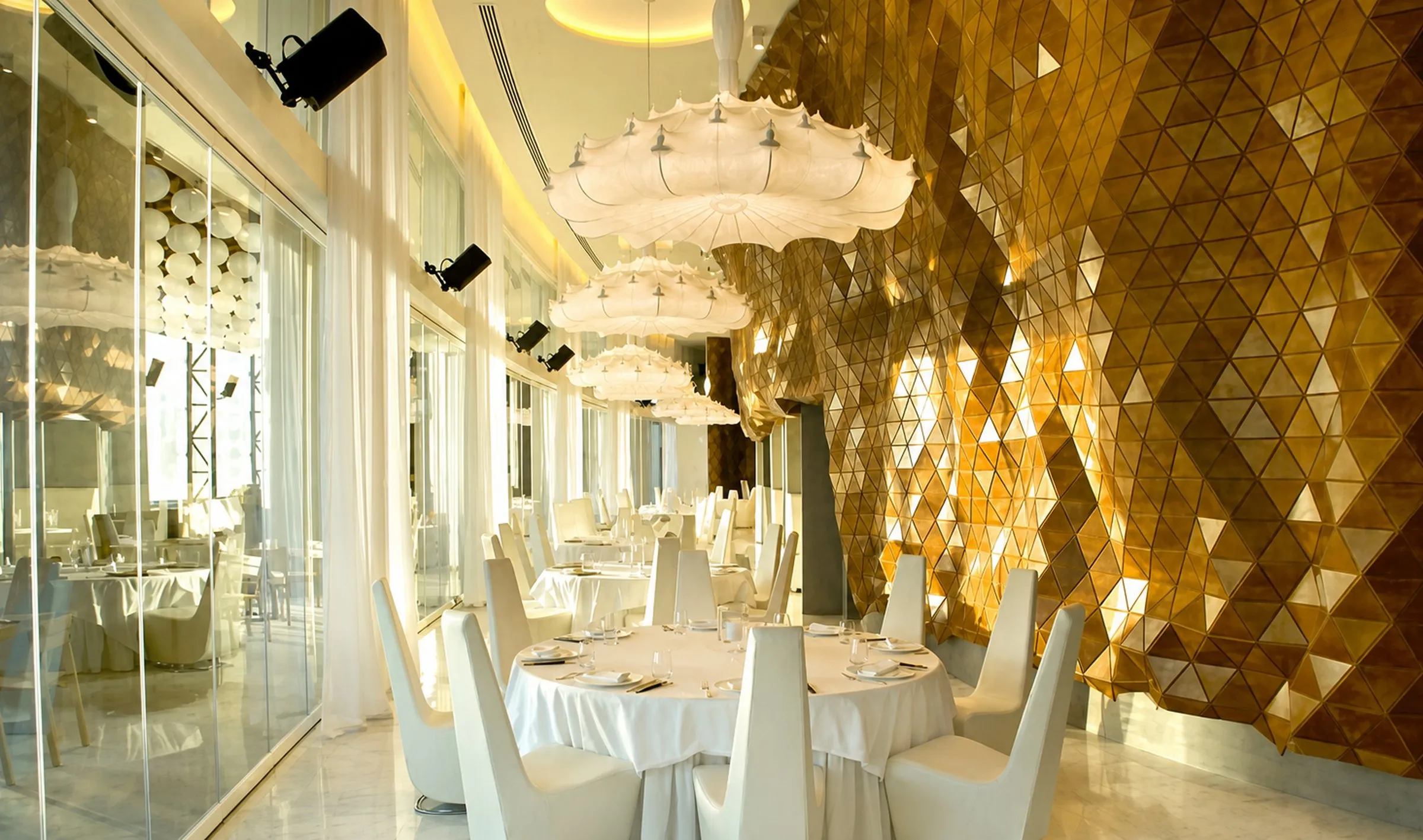 Dining room with a gold faceted feature wall, white table linen and a sculptural chandelier